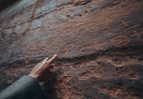 a person pointing at a rock with writing on it