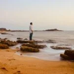 man in white shirt standing on brown sand near body of water during daytime