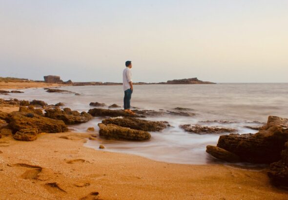 man in white shirt standing on brown sand near body of water during daytime