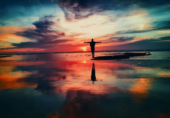 silhouette of person standing on rock surrounded by body of water