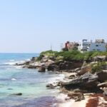 a view of a beach with houses on the cliff